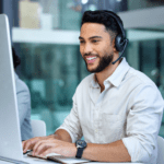 Smiling costumer support employee with headset, at their laptop.